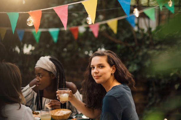 portrait of confident young woman holding drink while sitting at table during garden party - garden decoration stock pictures, royalty-free photos & images