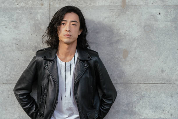 portrait of cool young handsome man wearing leather jacket and leaning against concrete wall - fashion stock pictures, royalty-free photos & images