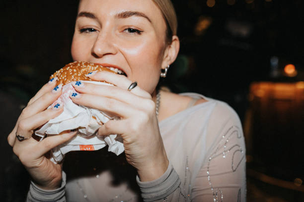 portrait of hungry woman taking bite of burger at bar - junk food stock pictures, royalty-free photos & images