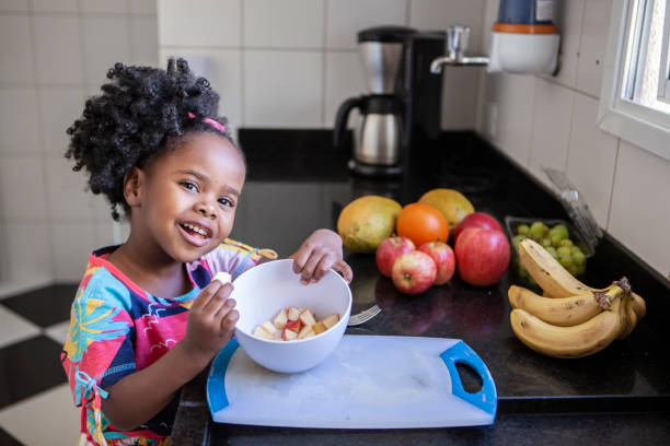 portrait of little girl eating fruits in the kitchen - food stock pictures, royalty-free photos & images