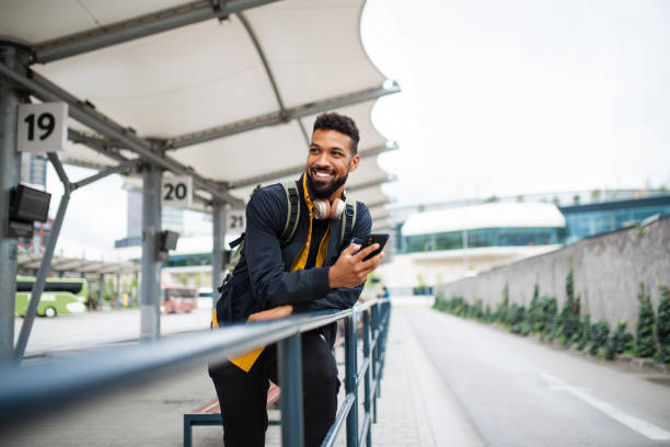 portrait of man commuter at the bus station using smartphone and waiting for bus. - travel stock-fotos und bilder