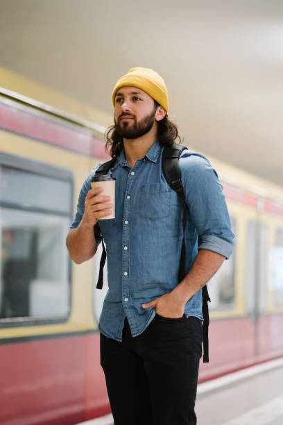 portrait of man with backpack and coffee to go waiting at platform, berlin, germany - junk food stock pictures, royalty-free photos & images