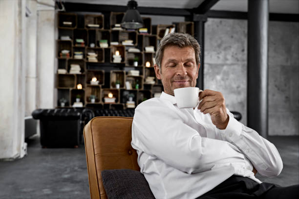 portrait of mature man enjoying cup of coffee in loft - coffee stockfoto's en -beelden