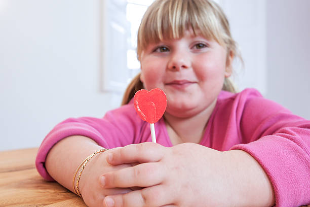 portrait of overweight girl holding heart shape lollipop - junk food stockfoto's en -beelden