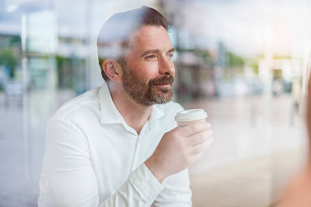 portrait of relaxed businessman looking through window of coffee shop - junk food stock pictures, royalty-free photos & images