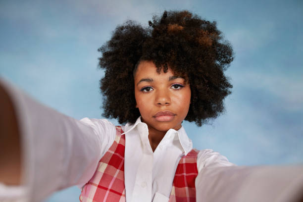 portrait of serious teenage girl with afro hairstyle taking selfie against colored background - hairstyle stock pictures, royalty-free photos & images