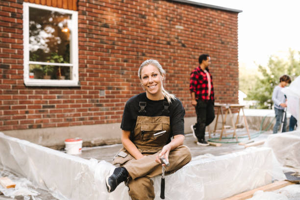 portrait of smiling mother sitting on concrete while family working in background during summer - home decoration stockfoto's en -beelden