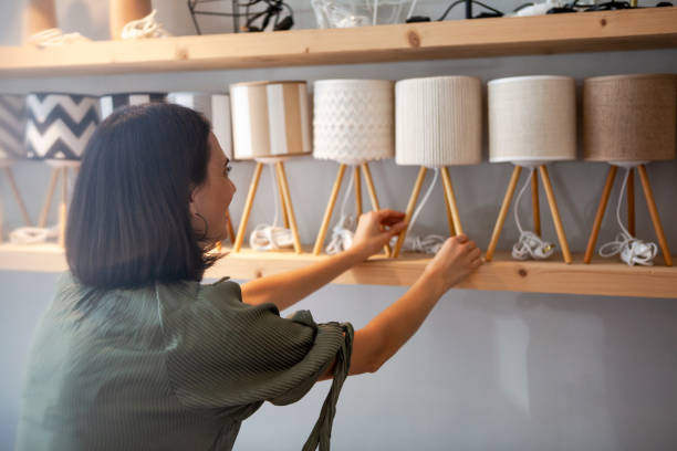 portrait of young adult woman arranging night table lamps at deco store - home decoration stock pictures, royalty-free photos & images