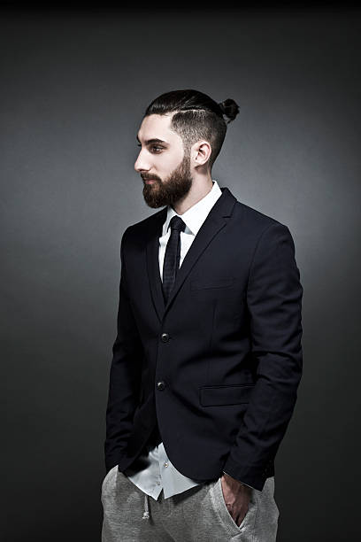 portrait of young man wearing black jacket and jogging pants in front of grey background - hairstyle stock pictures, royalty-free photos & images