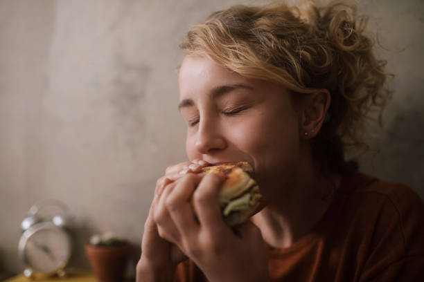 portrait of young woman eating hamburger - junk food stock pictures, royalty-free photos & images