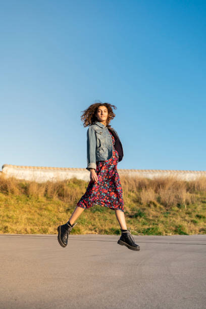 portrait of young woman with curly brown hair jumping in the air - fashion stock pictures, royalty-free photos & images