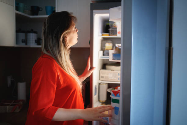 pregnant woman in front of the open fridge in the middle of the night - junk food stock pictures, royalty-free photos & images