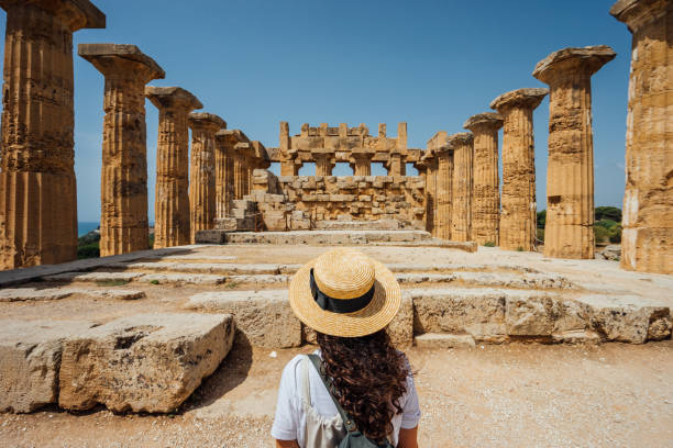 rückansicht einer frau mit hut, während sie einen antiken tempel in sizilien bewundert - travel stock-fotos und bilder