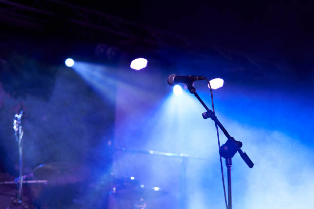 rear view low angle view of a microphone and spotlights on stage at a live concert with musical instruments background - concert stock pictures, royalty-free photos & images