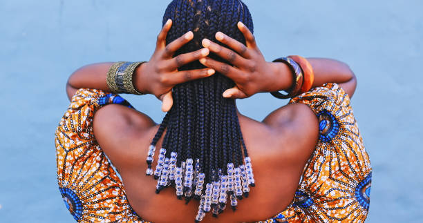 rearview shot of a young woman wearing traditional african clothing and feeling her hair against a blue background - hairstyle stock pictures, royalty-free photos & images