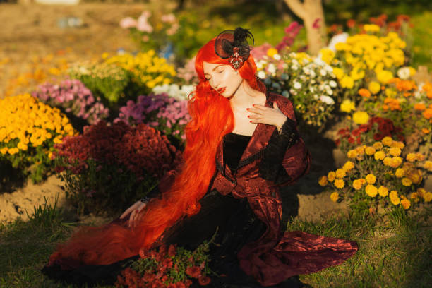 redhead woman in red gothic dress in garden. halloween style. long hair. autumn - garden decoration stock pictures, royalty-free photos & images