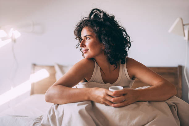 relaxed woman enjoying morning coffee in cozy bedroom - coffee stockfoto's en -beelden