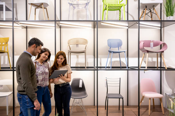 retail clerk helping a couple buying chairs at a furniture store - home decoration stock pictures, royalty-free photos & images