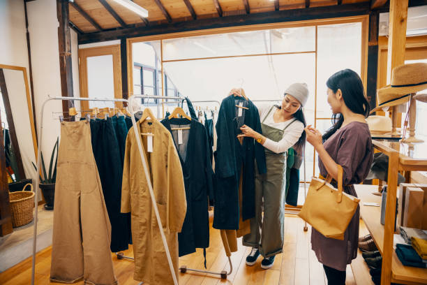retail shop clerk helping a mid adult woman customer shop for clothing in a boutique - fashion stock pictures, royalty-free photos & images