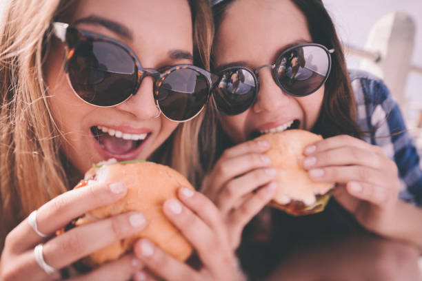 retro style shot of teenage girl best friends eating burgers - junk food stock pictures, royalty-free photos & images