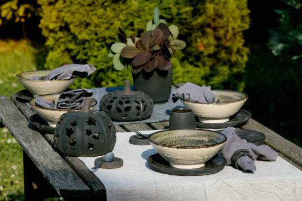 Rustic table setting outside in garden with empty craft ceramic tableware, black plates and rough bowls, pumpkin decorations, on linen tablecloth...