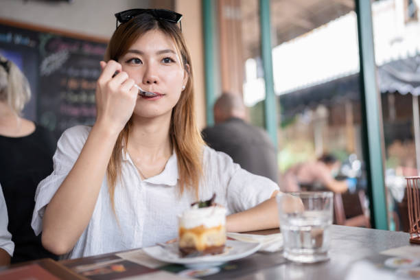 süßigkeiten geben ihrem körper energie und sorgen für erfrischung. junge koreanerin, die im café sitzt und ein stück kuchen und kaffee zur entspannung isst, nachdem sie den tempel in bangkok besichtigt hat. essen und trinken 