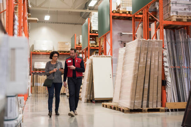 salesman and female customer using smart phone while walking in hardware store - home decoration stock pictures, royalty-free photos & images