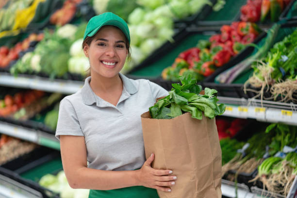 saleswoman holding a home delivery order in a paper bag smiling at camera - junk food stock pictures, royalty-free photos & images