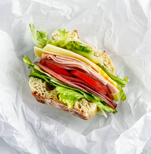 sandwiche with salami, ham, cheese, and tomatoes on parchment paper - junk food stock pictures, royalty-free photos & images