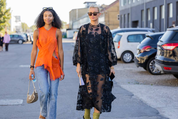 Sara Flaaen Licius wearing orange top, denim jeans & Andrea Steen wearing black sheer dress seen outside Henrik Vibskov during Copenhagen Fashion...