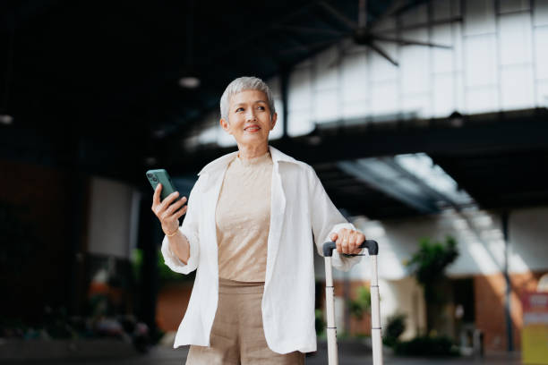 senior asian female business traveller using smartphone - travel stock pictures, royalty-free photos & images