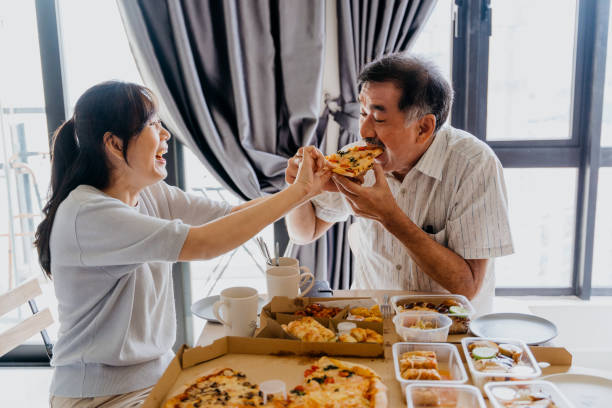 senior couple eating pizza at home - junk food stock pictures, royalty-free photos & images