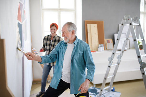 senior couple indoors at home renovating home, painting wall. - home decoration stock pictures, royalty-free photos & images