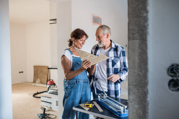 senior couple laying tile floor in new home, using manual cutter. - home decoration stock pictures, royalty-free photos & images