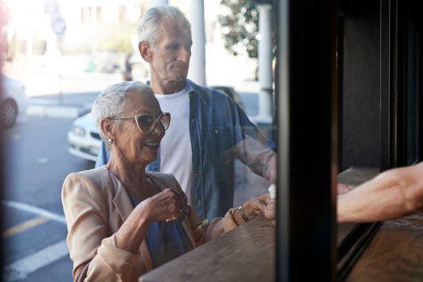 senior couple ordering coffee to-go, at street bakery - junk food stock pictures, royalty-free photos & images