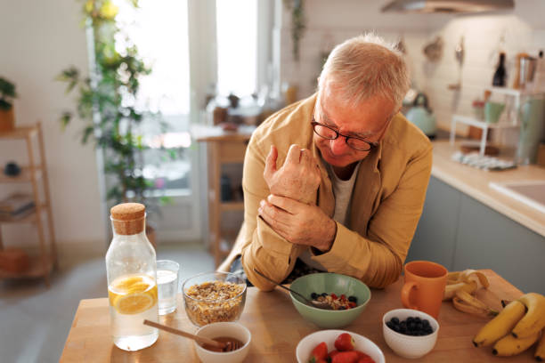 senior man experiencing hand joint pain while having breakfast in the kitchen - food stock pictures, royalty-free photos & images