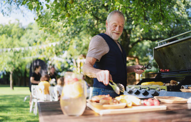 senior man on outdoor summer barbecue garden party, preparing food on grill. - garden decoration photos et images de collection