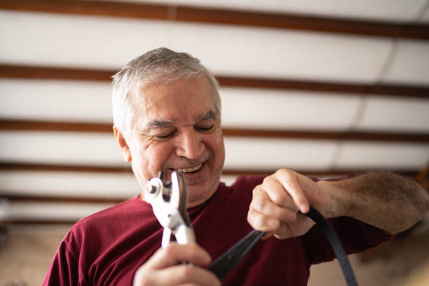 senior man using a leather awl on a belt at home - home decoration stock pictures, royalty-free photos & images