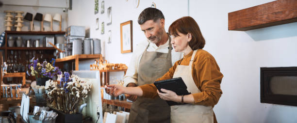 senior white couple work together at own small business retail shop. discuss talk using digital tablet, computer. sell art and craft home decor product. adult business people, sme entrepreneur concept - home decoration stock 