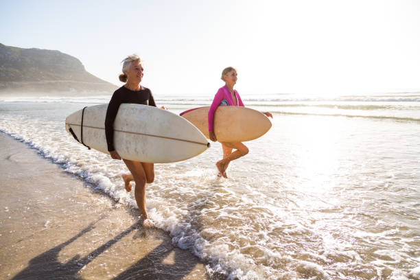 senior women going for a morning surf in the sea - travel stock pictures, royalty-free photos & images