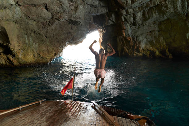 shirtless young man jumping in sea - travel stock pictures, royalty-free photos & images