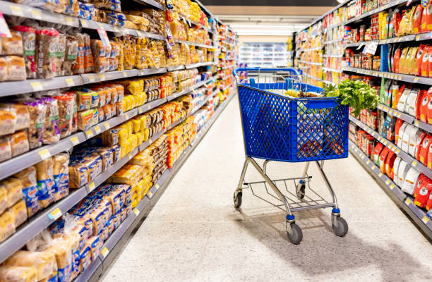 shopping cart in the aisle of a supermarket - junk food stock pictures, royalty-free photos & images