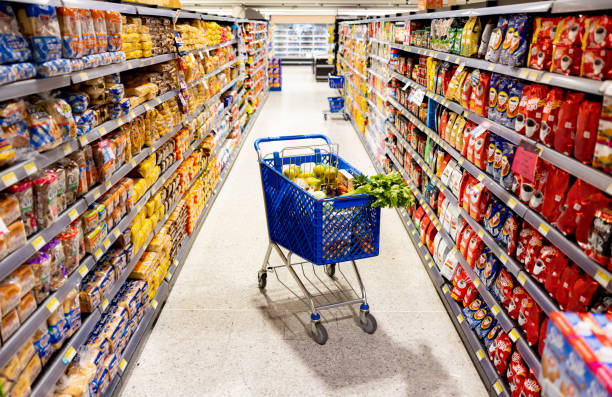 shopping cart in the middle on an aisle at the supermarket - junk food stock pictures, royalty-free photos & images