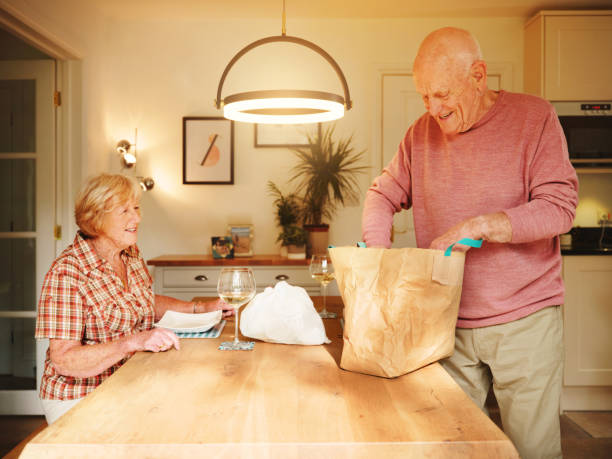 shot of a senior man unpacking takeout food from a paper bag to enjoy with his wife at home - junk food stock pictures, royalty-free photos & images