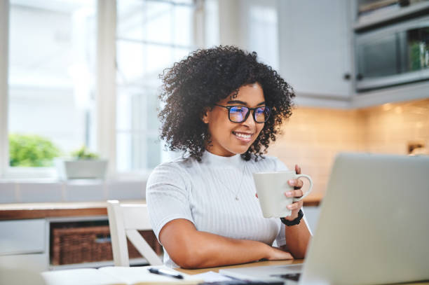 shot of a young woman using a laptop and having coffee while working from - coffee stockfoto's en -beelden