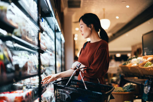 side profile of beautiful young asian woman carrying a shopping basket, grocery shopping for daily necessities in supermarket. healthy eating lifestyle. making healthier food choices - food fotografías e imágenes de stock
