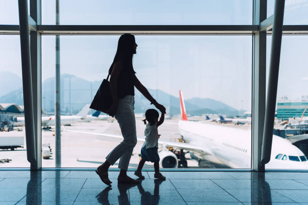 silhouette of joyful young asian mother holding hands of cute little daughter looking at airplane through window at the airport while waiting for departure - travel stockfoto's en -beelden