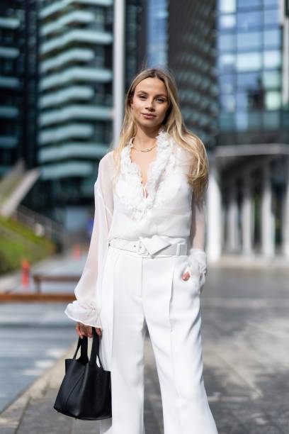 Simona Jakstaite wears a black leather bag, a white long sleeved shirt and white high waist wide leg trousers outside Ermanno Scervino show during...