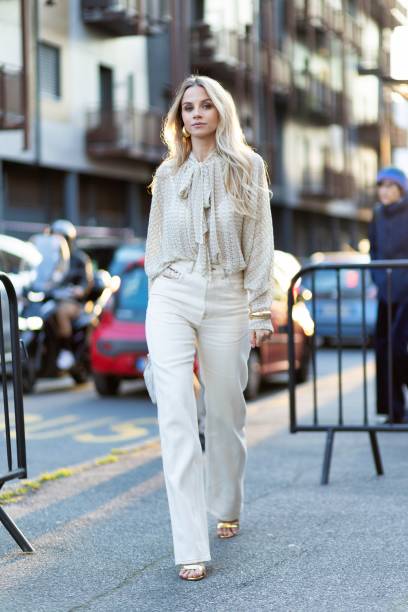 Simona Jakstaite wears gold heeled sandals, gold hoop earrings, a beige Missoni long sleeved shirt, gold bracelets, a white cream Bottega Veneta...