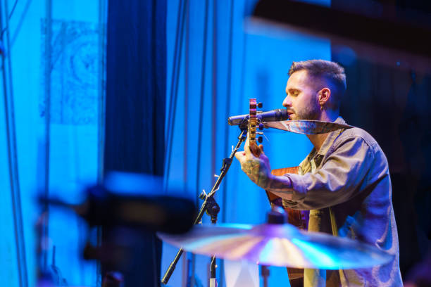 singer playing guitar and singing on stage during a concert - concert photos et images de collection